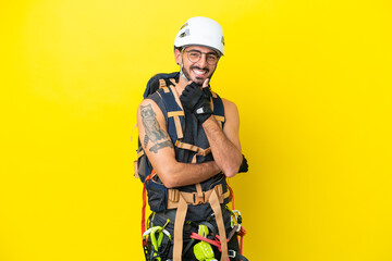 Young caucasian rock climber man isolated on yellow background with glasses and smiling