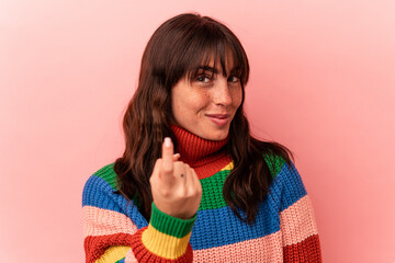 Young Argentinian woman isolated on pink background pointing with finger at you as if inviting come closer.