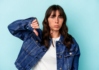 Young Argentinian woman isolated on blue background showing a dislike gesture, thumbs down....