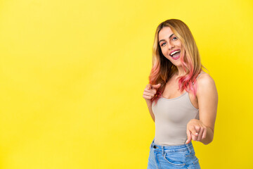 Young woman over isolated yellow background surprised and pointing front