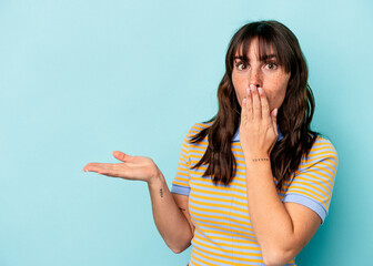 Young Argentinian woman isolated on blue background impressed holding copy space on palm.