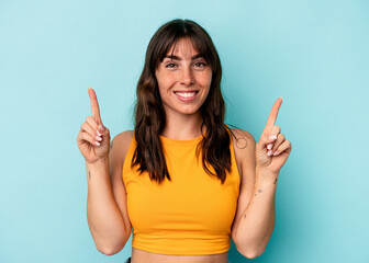 Young Argentinian woman isolated on blue background indicates with both fore fingers up showing a...
