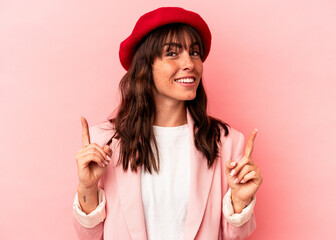 Young Argentinian woman isolated on pink background indicates with both fore fingers up showing a...