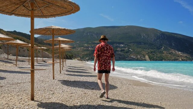 Rear View Of A Man Wearing Hat And Floral Shirt Walking On A Sandy Shore Enjoying His Summer Vacation At Agia Kiriaki Beach Near Zola Village In Kefalonia, Greece. - Static Shot