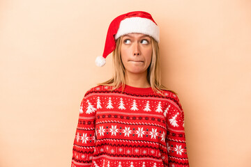 Young caucasian woman celebrating Christmas isolated on beige background confused, feels doubtful and unsure.