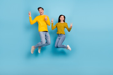Full size photo of carefree spouses married youth jump make v-sign isolated over blue color background