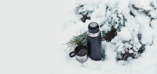 termos z gorącą kawą i termokubkiem w zimowym lesie. 