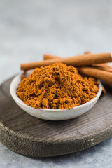 Ceylon cinnamon sticks with cinnamon powder in wooden bowl on concrete background.