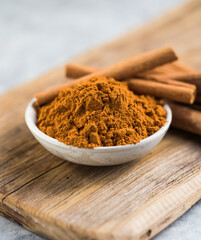 Ceylon cinnamon sticks with cinnamon powder in wooden bowl on concrete background.