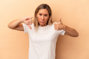Young caucasian woman isolated on beige background showing thumbs up and thumbs down, difficult...