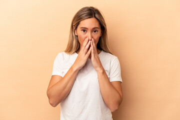 Young caucasian woman isolated on beige background covering mouth with hands looking worried.
