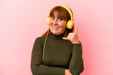 Middle age caucasian woman listening to music isolated on pink background showing a mobile phone call gesture with fingers.