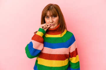 Middle age caucasian woman wearing a multicolor sweater isolated on pink background with fingers on lips keeping a secret.