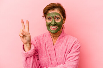 Middle age caucasian woman wearing a facial mask isolated on pink background showing number two with fingers.