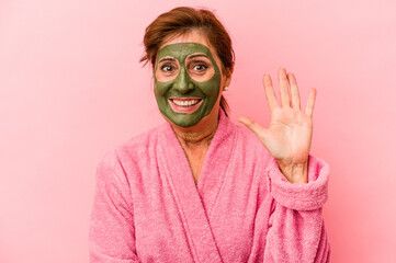 Middle age caucasian woman wearing a facial mask isolated on pink background smiling cheerful showing number five with fingers.