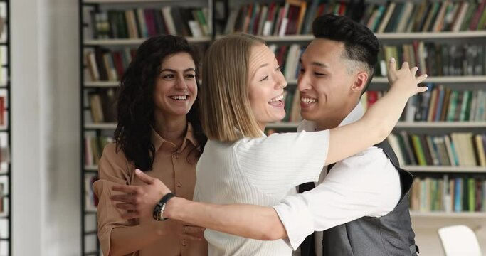 Three excited diverse students girls and guy embracing greet each other meet in library of university. Concept of best friends bond, good warm friendly relationships of multi ethnic schoolmates, amity
