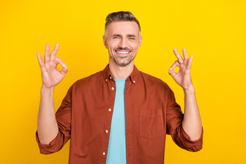 Photo of funky young white hairdo man show okey wear brown shirt isolated on vivid yellow color background