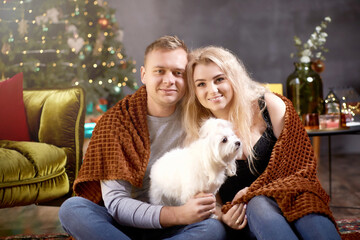 Lovely romantic couple in festive aesthetic cozy home interior with their dog near Christmas tree. Candid, true moment. Good mood and having fun together. Christmas love story