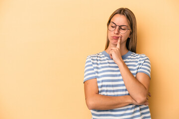 Young caucasian woman isolated on yellow background looking sideways with doubtful and skeptical expression.