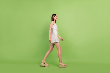Full length profile photo of cute young brunette lady go wear overall sandals isolated on green...