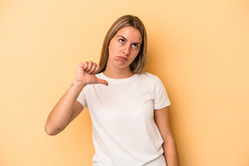 Young caucasian woman isolated on yellow background showing a dislike gesture, thumbs down....