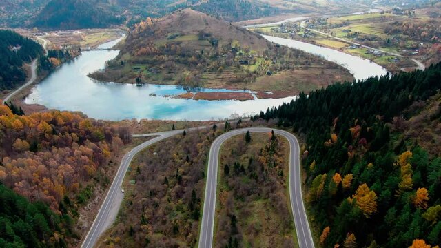 Flight over serpentine road in the mountains with river. Aerial view of the autumn mountains with mountain road serpentine, river and forest on the background. Carpathians. Footage from drone.