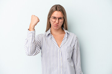 Young caucasian woman isolated on blue background showing fist to camera, aggressive facial expression.