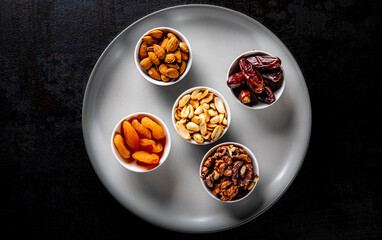 almonds, peanuts, walnuts, dates, dried apricots in a plate on Dark grey black slate background
