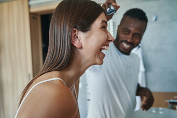 Smiling man shaving laughing woman forehead in bathroom
