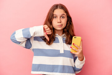 Little caucasian girl holding mobile phone isolated on pink background showing a dislike gesture, thumbs down. Disagreement concept.