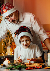 Vertical photo of a child preparing Christmas gingerbread cookies, together with grandpa in the home kitchen