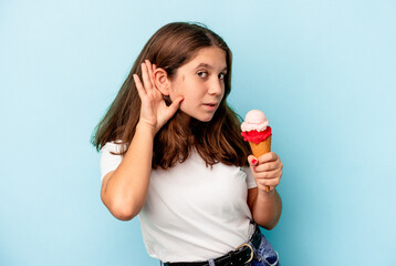 Little caucasian girl eating an ice cream isolated on blue background trying to listening a gossip.