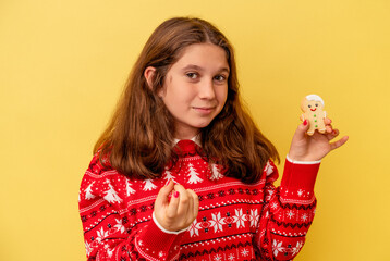 Little caucasian girl holding a Christmas cookies isolated on yellow background pointing with finger at you as if inviting come closer.