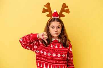 Little caucasian girl wearing a Christmas reindeer hat isolated on yellow background showing a dislike gesture, thumbs down. Disagreement concept.