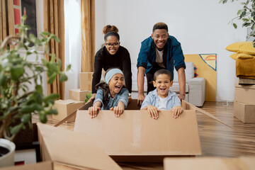 Parents have fun driving cute little son and beautiful daughter in cardboard box play in living room on relocation to new home family feel overjoyed involved in fun activities of moving in together