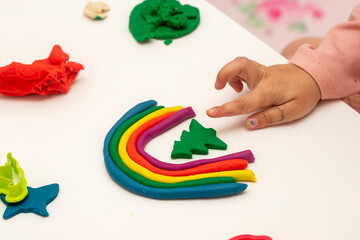 Girl playing dough. Girl making rainbow with dough on white background. Making various shapes with...