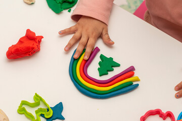 Girl playing dough. Girl making rainbow with dough on white background. Making various shapes with...