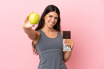 Young caucasian woman isolated on pink background taking a chocolate tablet in one hand and an...