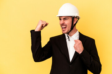 Young architect caucasian man isolated on yellow background raising fist after a victory, winner...