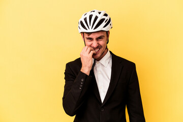 Young caucasian business man wearing a bike helmet isolated on yellow background biting fingernails, nervous and very anxious.