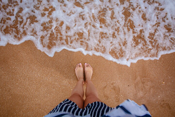 Woman's legs stand by the sea waves on a golden beach