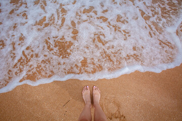 Woman's legs stand by the sea waves on a golden beach