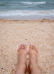 Woman's legs stand by the sea waves on a golden beach