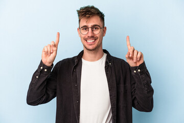 Young caucasian man isolated on blue background indicates with both fore fingers up showing a blank...