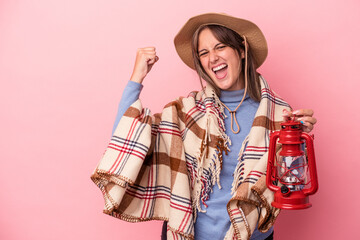 Young caucasian woman holding vintage lantern isolated on pink background raising fist after a victory, winner concept.