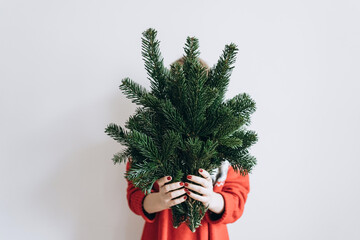 a modern woman in a red sweater with fir branches in her hands at Christmas on a light background. The minimum concept of the new year. no face