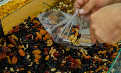 many different sweet dried fruits by weight. Male hand picks fruit with a spatula