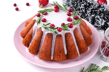 Christmas cake topped with sugar icing, cranberry and rosemary served on the plate. Dessert in festive table setting