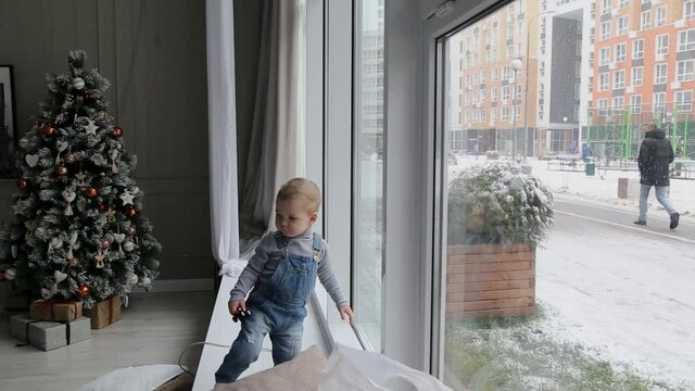 A little boy stands by the window in the winter during the Christmas holidays.