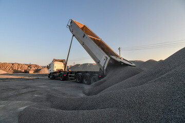 Heavy dump truck unloading gravel on industrial quarry production site.